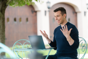 Matt Fraser sits at an outdoor table, gesturing expressively while using a laptop.