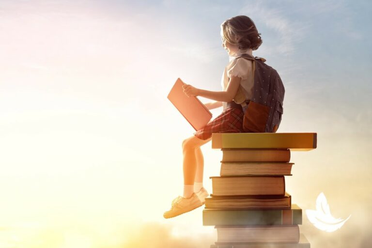 A young girl wearing a backpack sits on top of a stack of large books, reading a book, against a soft, glowing sky background.