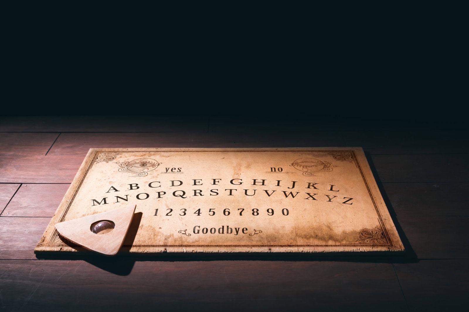 Ouija board on a wooden floor with a planchette resting near the lower left corner.